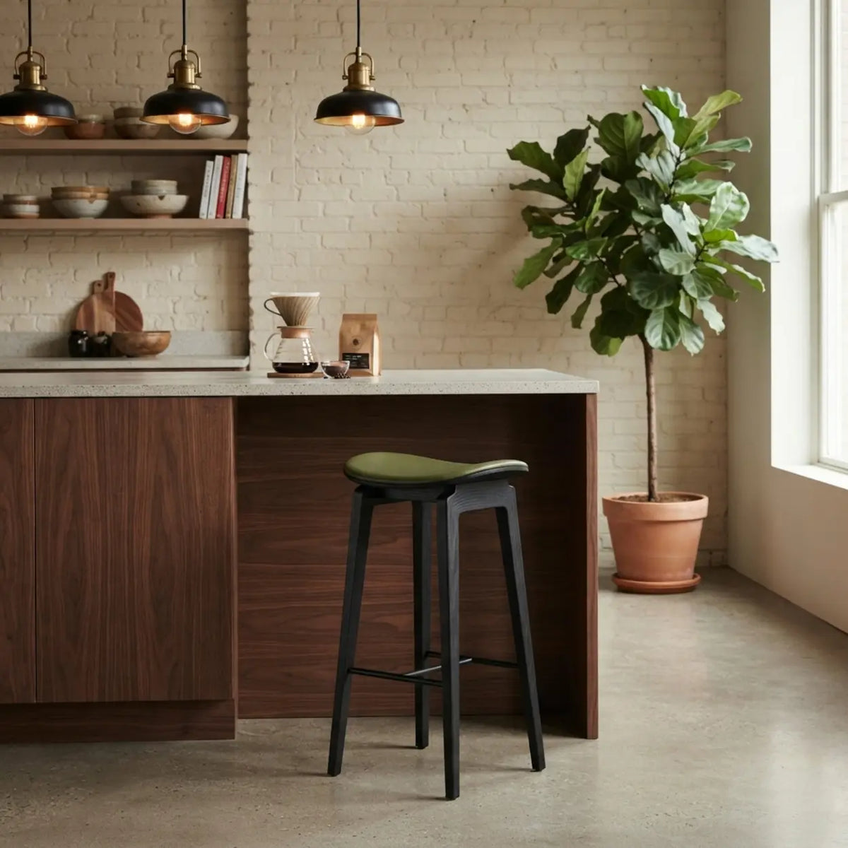 Green faux leather counter stool with a curved saddle seat, black wood frame and black footrest at a bright kitchen island