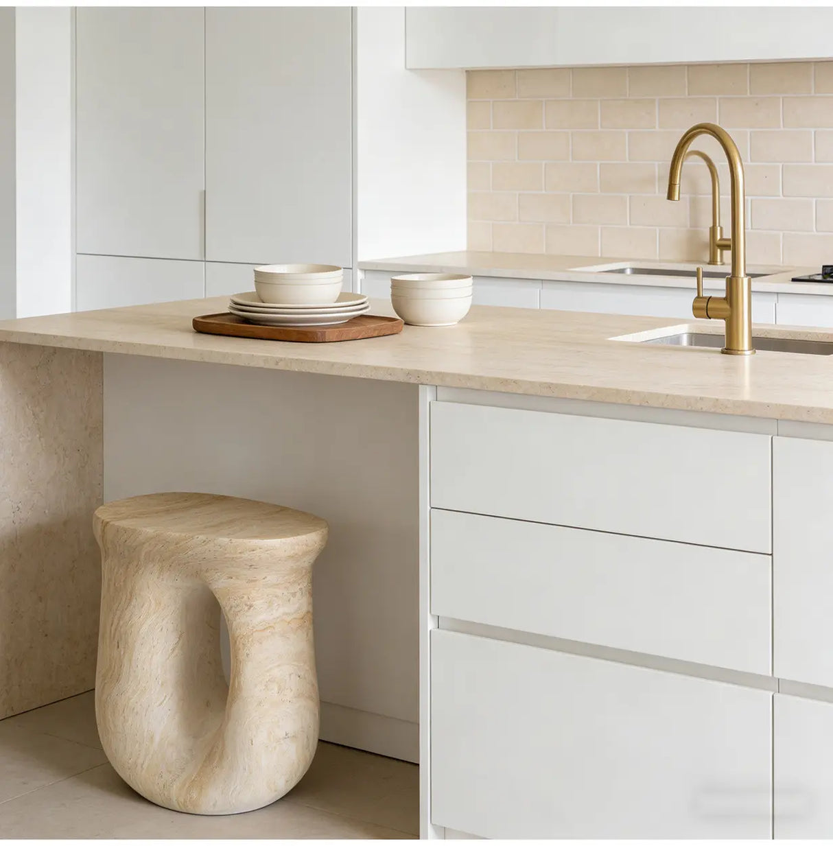 Faux travertine stone oval side table with a hollow curved base positioned beneath a bright modern kitchen island