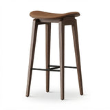 Brown faux leather counter stool with a curved saddle seat, wood frame and black metal footrest on a white background