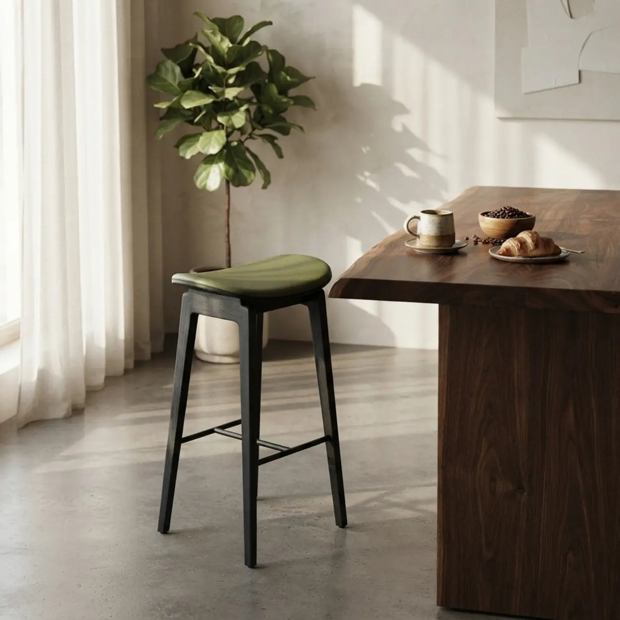 Green faux leather counter stool with a curved seat, black wood frame and black footrest beside a walnut kitchen island