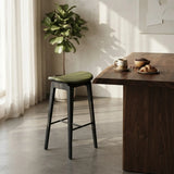 Green faux leather counter stool with a curved seat, black wood frame and black footrest beside a walnut kitchen island