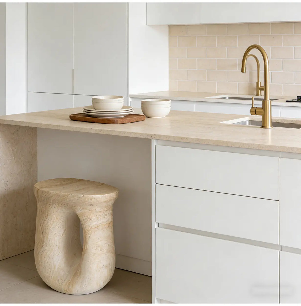 Faux travertine stone oval side table with a hollow curved base positioned beneath a bright modern kitchen island