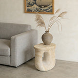 Faux travertine stone oval accent table with a curved open base beside a gray sofa, styled with a vase