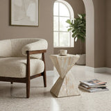 Travertine faux stone side table with a twisted geometric pedestal beside a boucle accent chair, styled with a cup and magazines