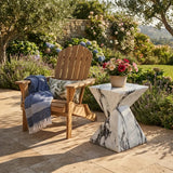 White veined faux stone side table with a twisted geometric pedestal on a stone patio beside a wicker lounge chair and flower pot