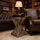 Brown stone side table with a twisted geometric pedestal in a home library between a leather sofa and armchair