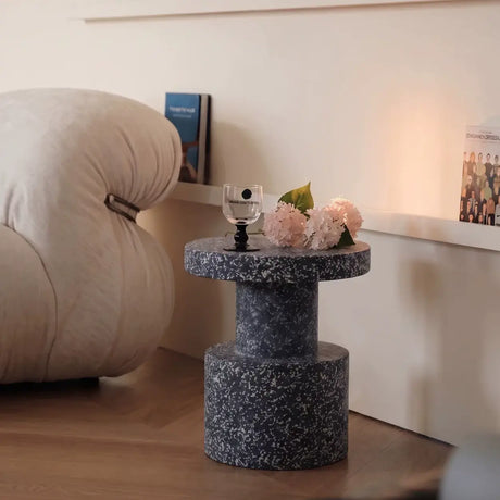 Round terrazzo side table in dark grey speckle with sculptural pedestal base, styled beside a beige living room armchair