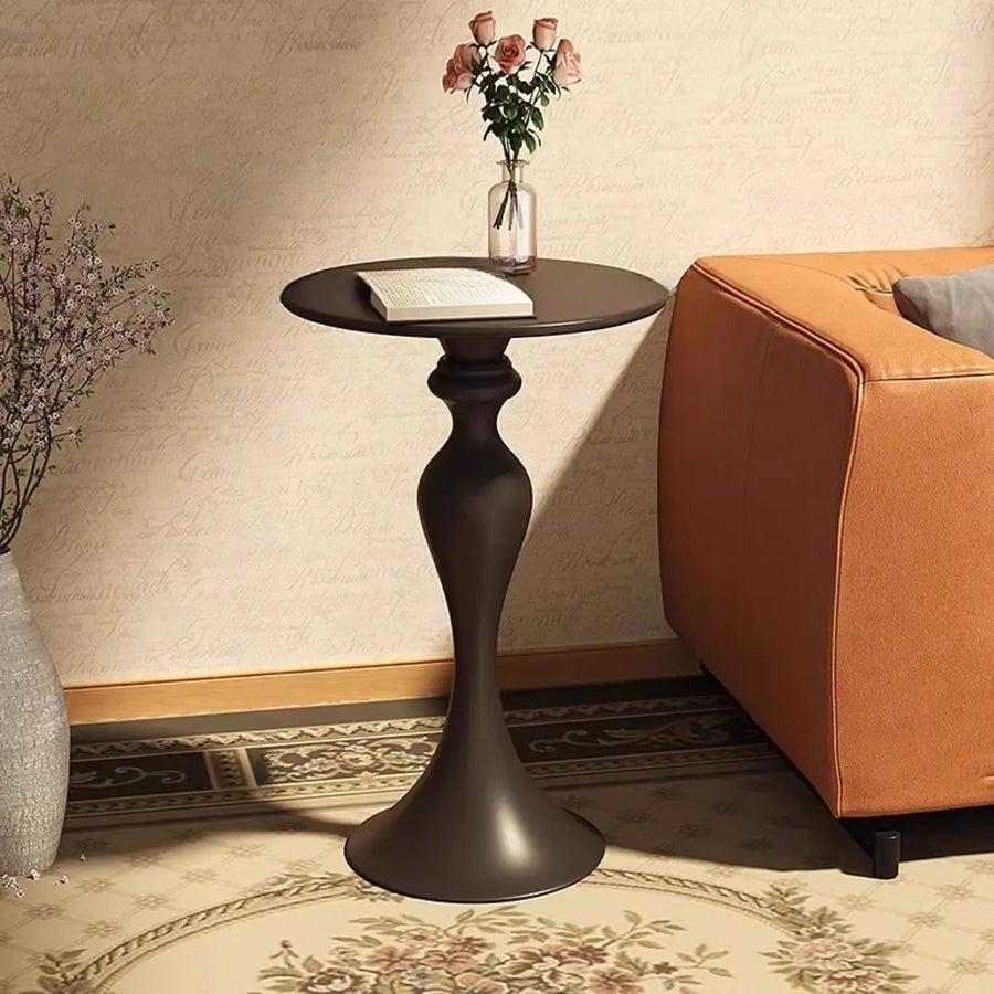 Small black sculpted pedestal side table beside living room seating