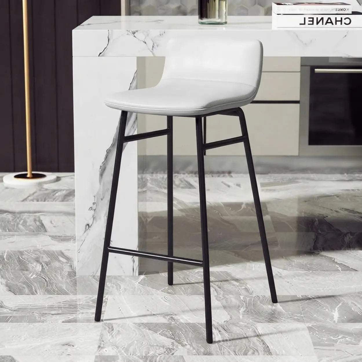 White faux leather counter stool with a contoured seat shell, matte black metal base and horizontal footrail beside a marble kitchen island